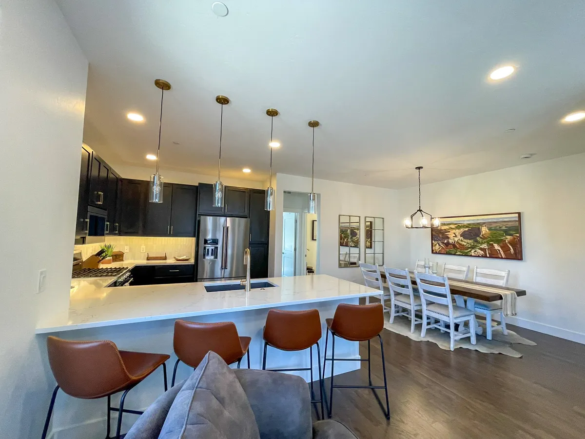 A welcoming kitchen and dining space with a central island, comfortable bar stools, pendant lights, and curated wall art. The dining table is set for a meal, and the kitchen is spacious and fully equipped, perfect for cooking or entertaining.