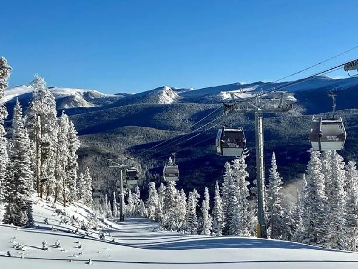 A sweeping exterior view of ski lift gondolas gliding above a snowy mountain landscape, surrounded by snow-laden trees. The scene evokes adventure, breathtaking scenery, and the thrill of outdoor winter sports.