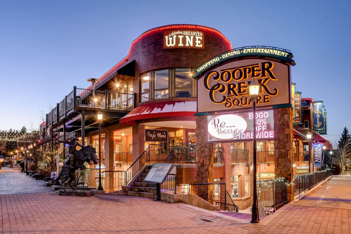A lively exterior scene in downtown Winter Park, featuring the Cooper Creek Square sign, wine shop, outdoor seating, and public art. The area is bustling with energy, highlighting social opportunities, dining, and dog-friendly patios mentioned in the section content.