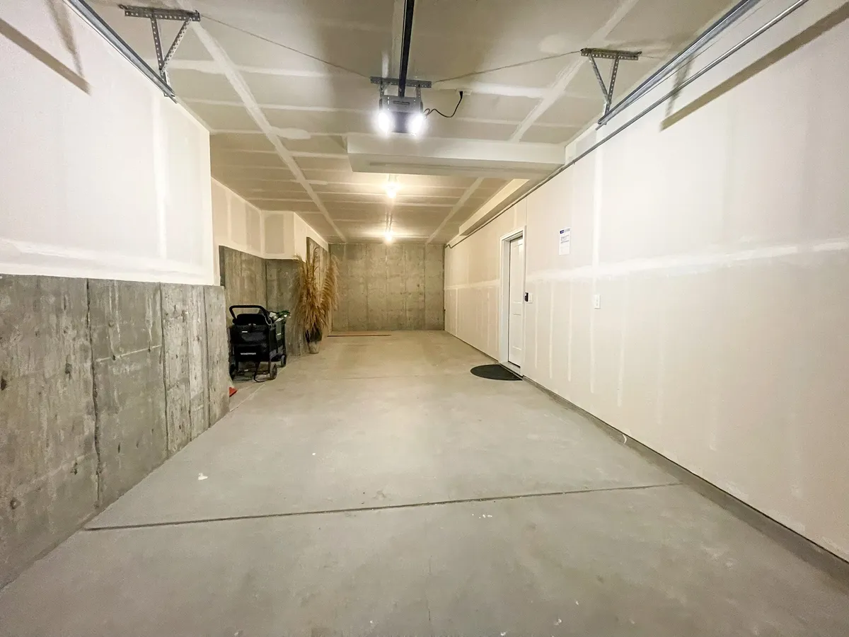 A spacious, well-maintained garage with concrete walls, a visible garage door opener, side entrance door, and organized storage area. The space feels functional and uncluttered, perfect for storing outdoor gear, vehicles, and adventure equipment.