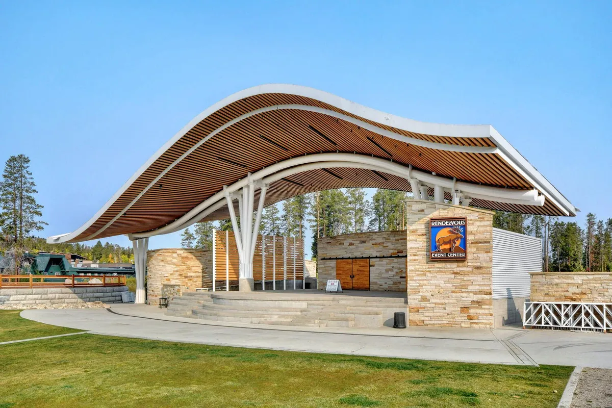 An exterior shot of The Foundry with its distinctive wavy roof, stone façade, and outdoor stage area, hinting at vibrant concerts and community events. The space is set for live performances or festive gatherings under the stars.