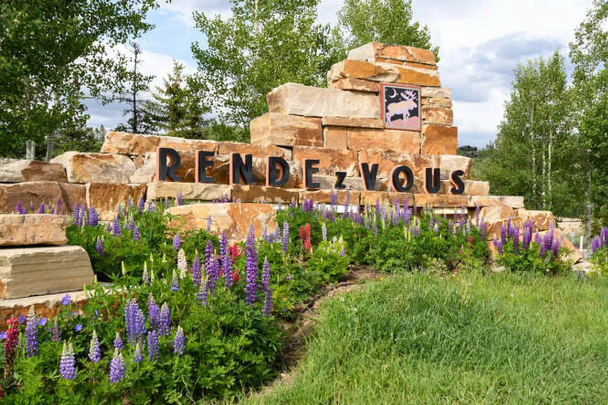 The image shows a beautiful landscaped area featuring a stone community sign, vibrant flowers, and green grass—suggesting proximity to open spaces and nature trails, perfect for dog walks and outdoor exploration.
