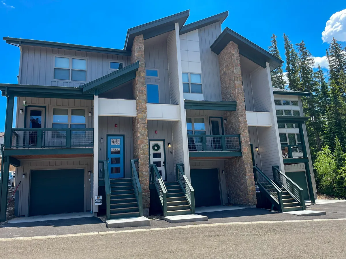 This exterior image showcases the property's modern architectural design, with stone accents and green trim, set against a backdrop ideal for mountain adventures. The scene implies proximity to outdoor activities like winter sports and community gatherings.