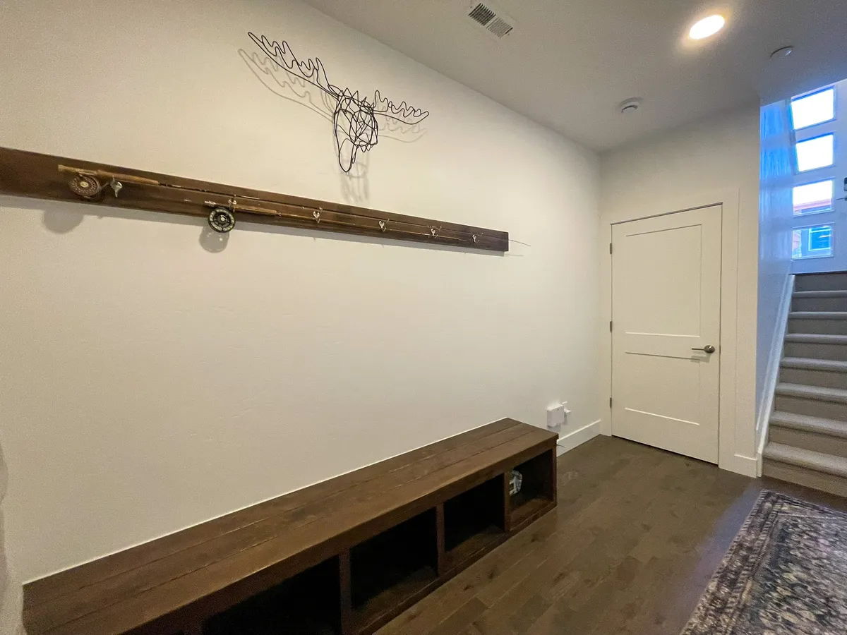 A rustic entryway featuring a wooden bench, coat rack with hooks, and a decorative moose head. The scene suggests a welcoming spot for guests to gear up or wind down after outdoor adventures.
