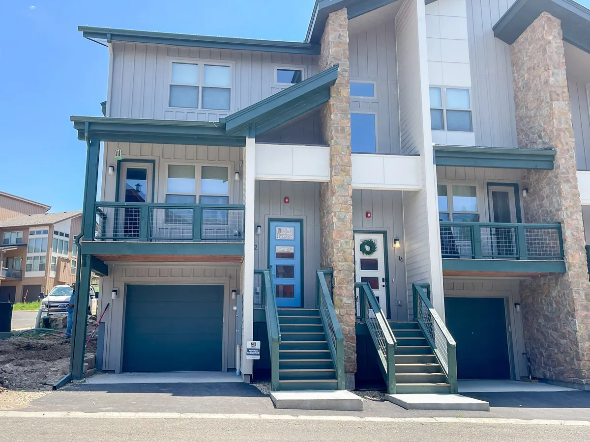 This exterior image captures the welcoming front entry of the chalet with stone columns, balconies, a staircase, and a cheerful front door adorned with a wreath. The scene hints at a comfortable retreat surrounded by nature, ideal for coming and going during outdoor adventures with your dog.