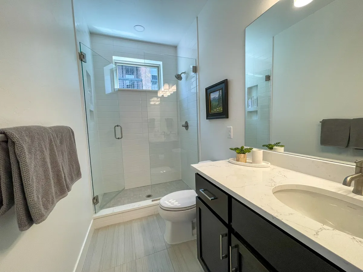 A modern ensuite bathroom with a glass shower enclosure, marble countertop vanity, window for natural light, and tasteful decorative details. The setting exudes serenity and spa-like luxury.